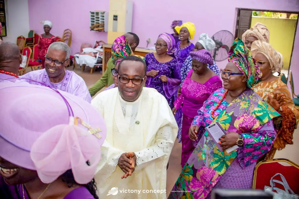 Guests in colorful traditional attire — purple, pink, and gold — gathered indoors for a ceremony, event styled by Victony Event Planners