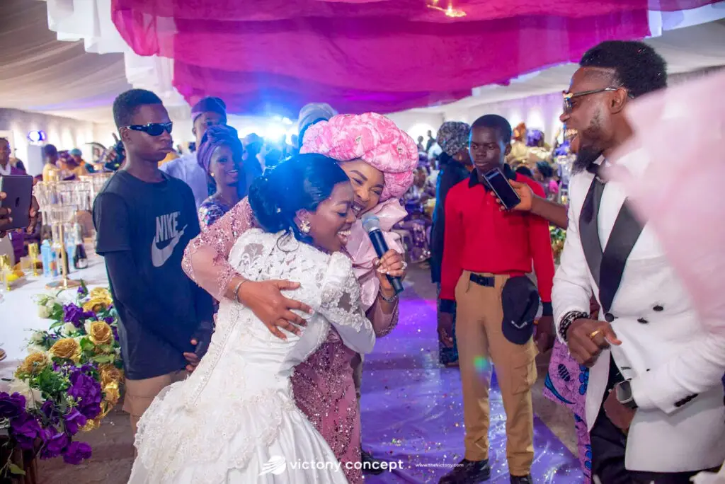 Bride embracing a guest on the dance floor at a wedding reception with purple lighting and floral decor, styled by Victony Event Planners